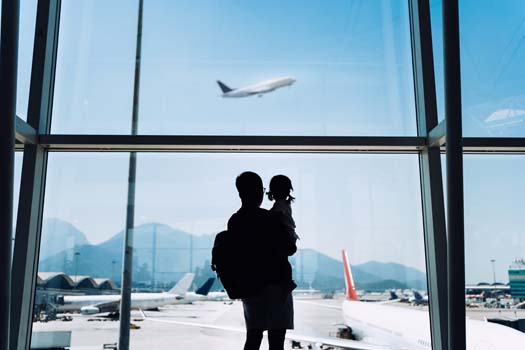 Silhouette of joyful young Asian father carrying cute little daughter looking at airplane through window at the airport while waiting for departure